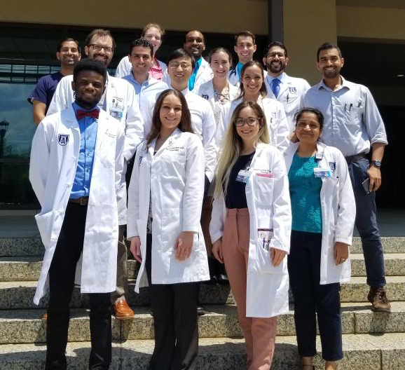 Group of residents in white coats standing on stairs in front of building