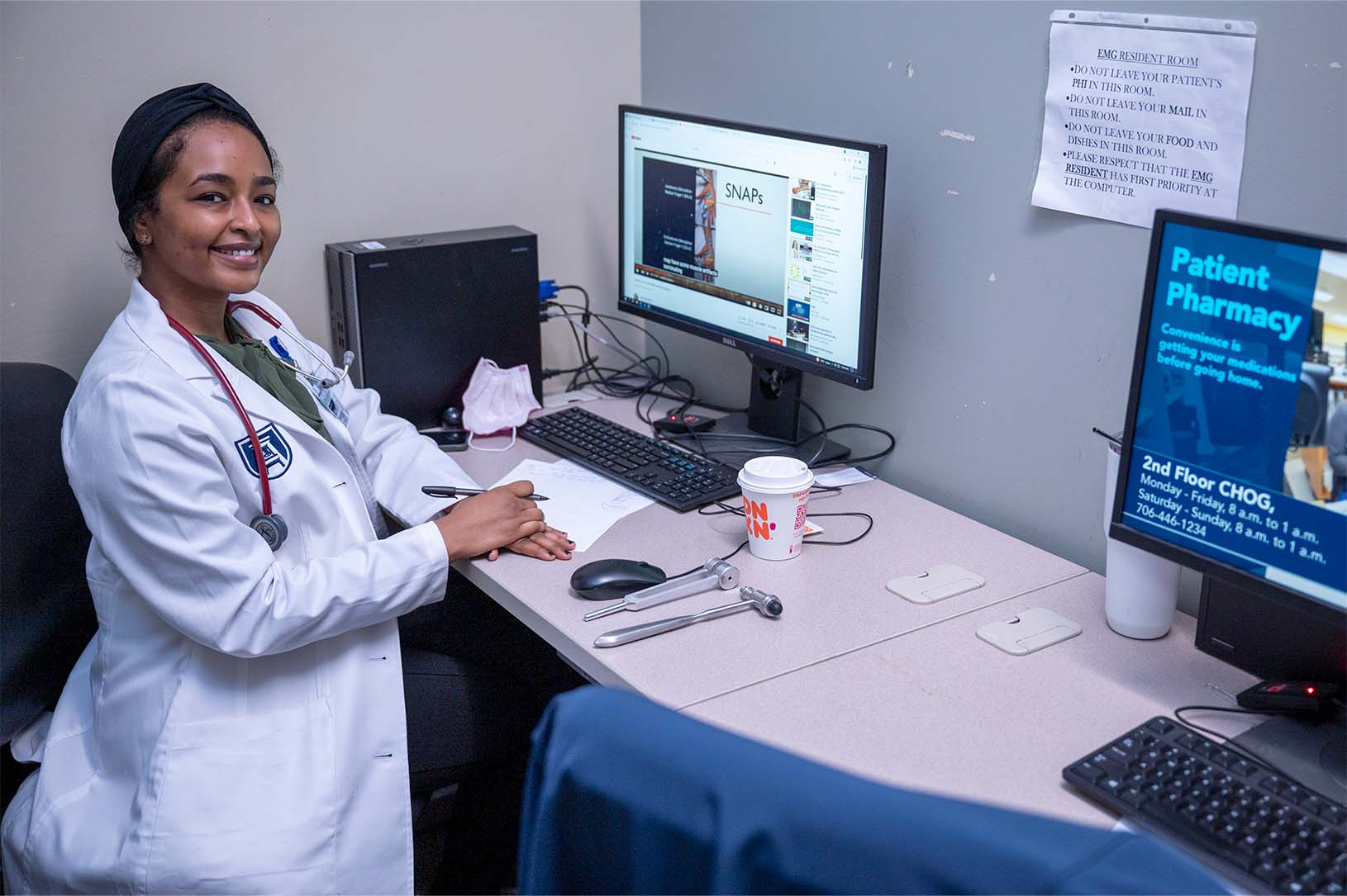 Woman standing in front of a computer turns to smile and look at us 